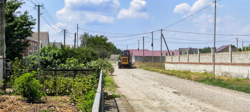 Дорожная техника на щебёночной улице среди домов и огородов