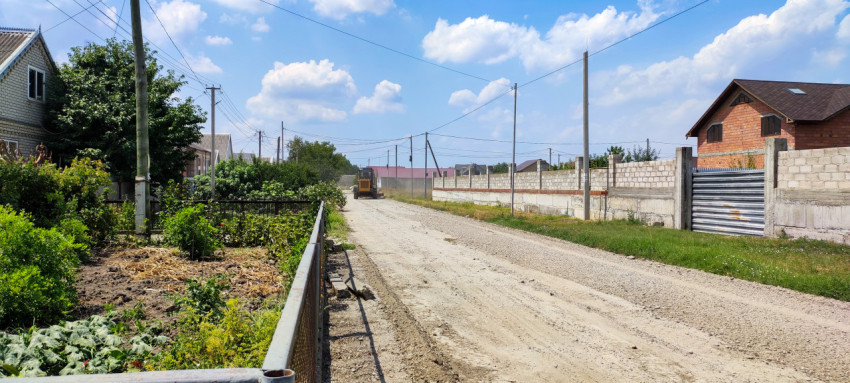 Грейдер на грунтовой дороге в частном секторе под голубым небом