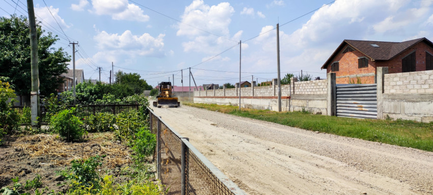 Автогрейдер на улице частного сектора во время ремонта грунтовой дороги