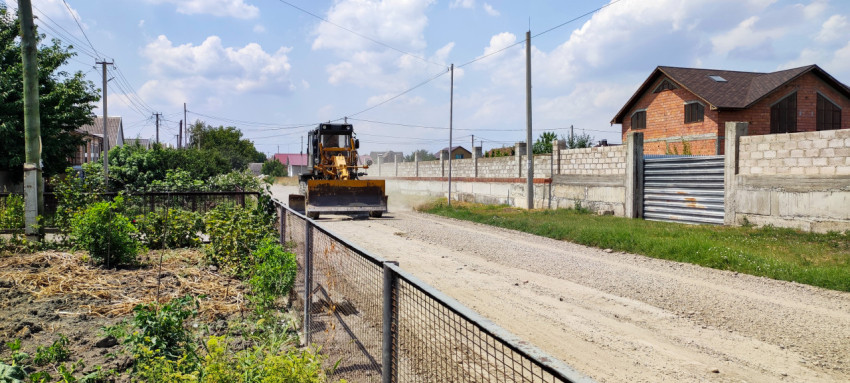 Дорожный грейдер с отвалом на щебёночной улице рядом с жилыми домами