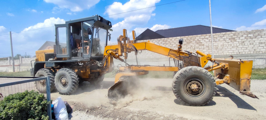 Боковой вид автогрейдера при выравнивании щебёночной дороги