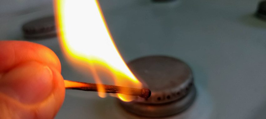Зажжённая спичка на фоне газовой плиты