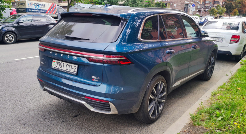 Задняя часть синего кроссовера Geely с видимым автомобильным номером на улице