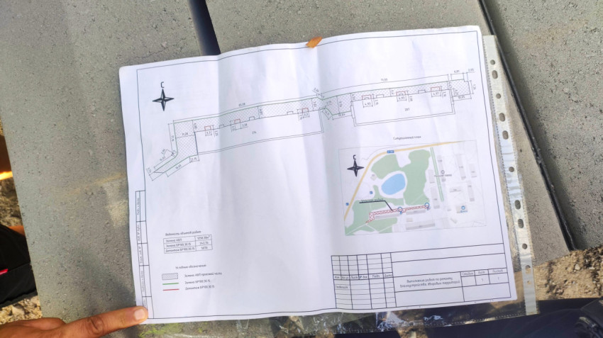 Лист строительного плана с чертежом и схемой расположения объекта в прозрачной папке на бетонной поверхности