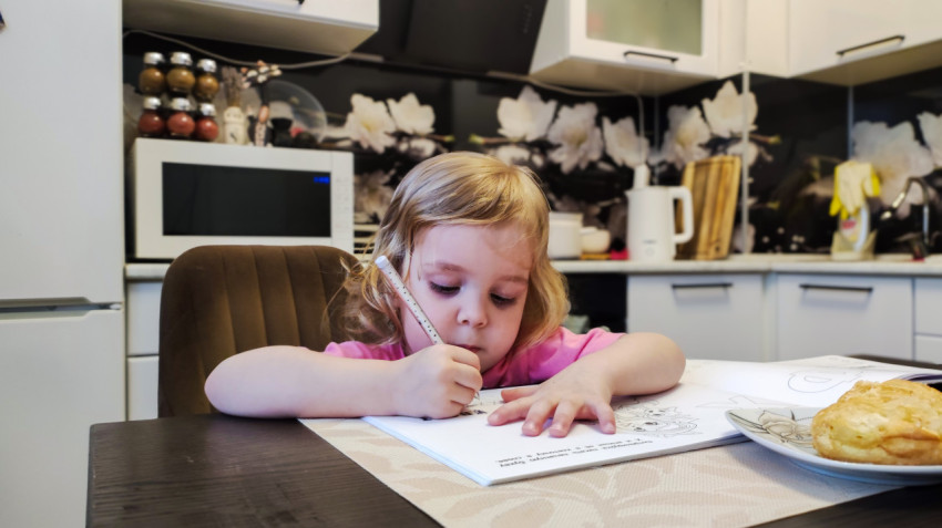 Девочка рисует карандашом за столом на кухне