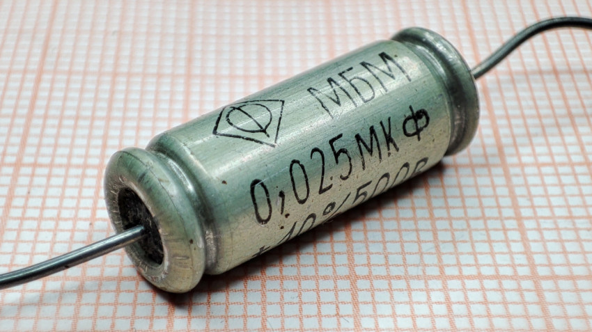 Металлобумажный конденсатор МБМ 0.025 мкФ на фоне миллиметровой бумаги