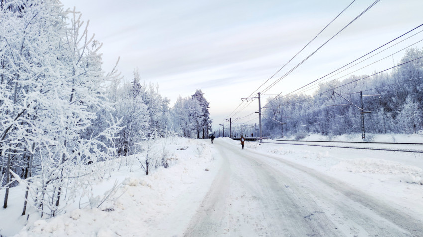 Идущий пешеход на зимней дороге у железнодорожных рельсов