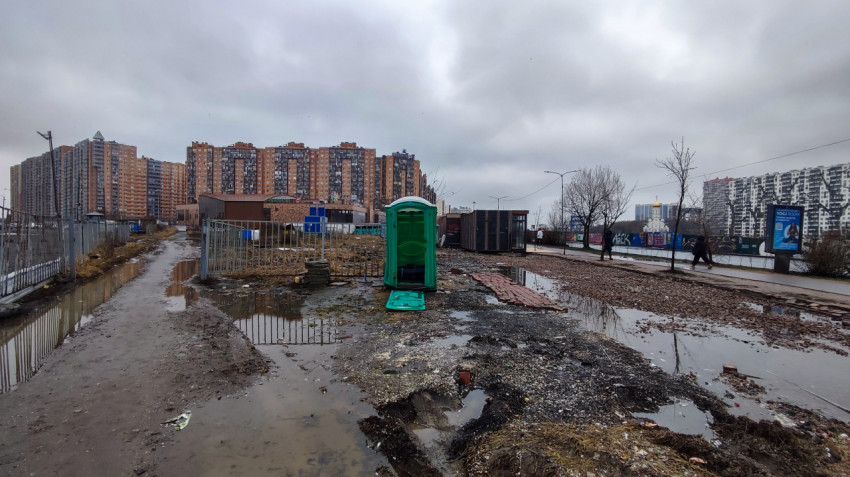 Биотуалет с упавшей дверцей на фоне городских домов