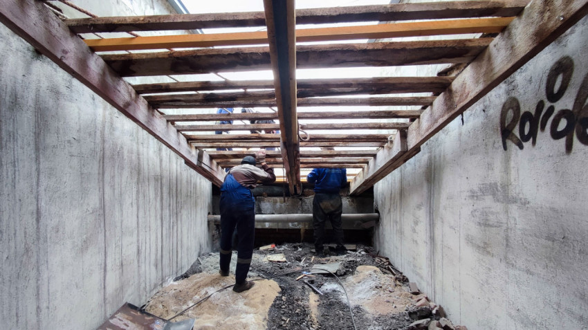 Рабочие устанавливают балки в открытом приямке между стенами