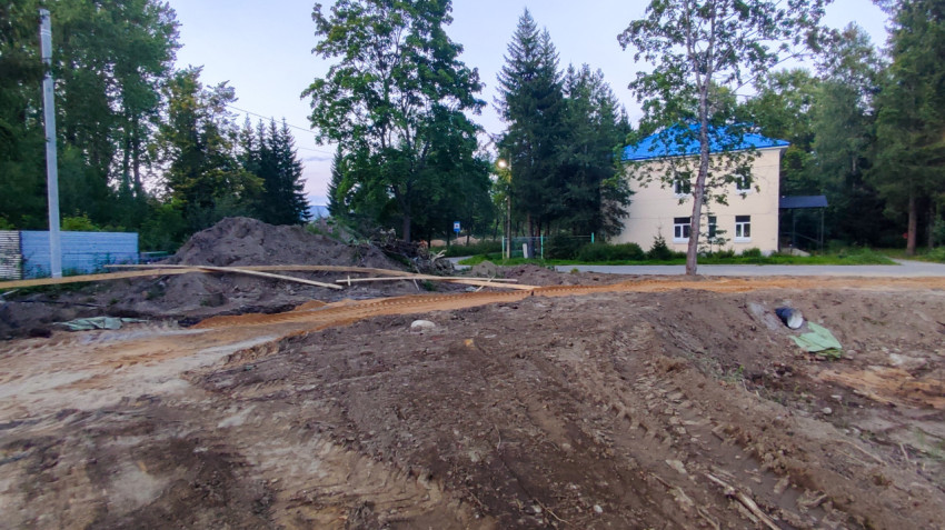 Земляные работы с отвалами грунта рядом со зданием на фоне деревьев