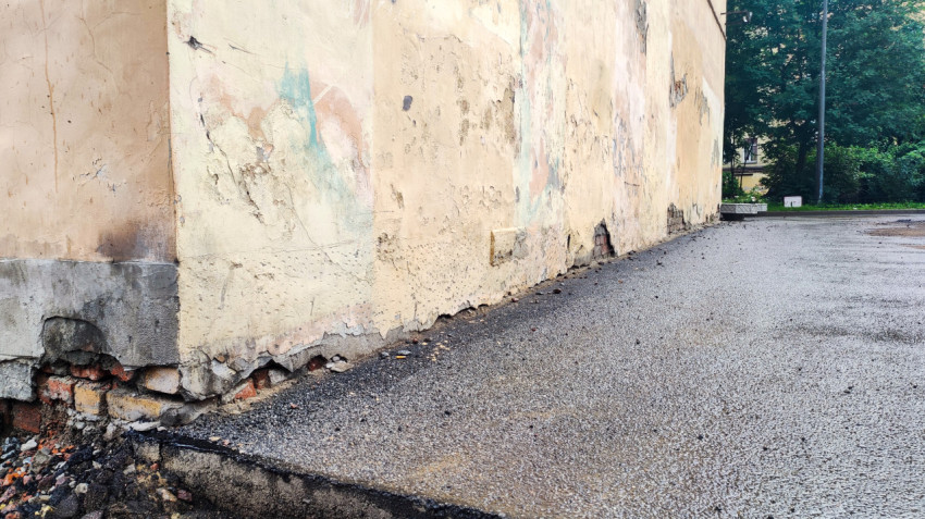Угол фасада с отслаивающейся штукатуркой и асфальтовым проходом вдоль здания