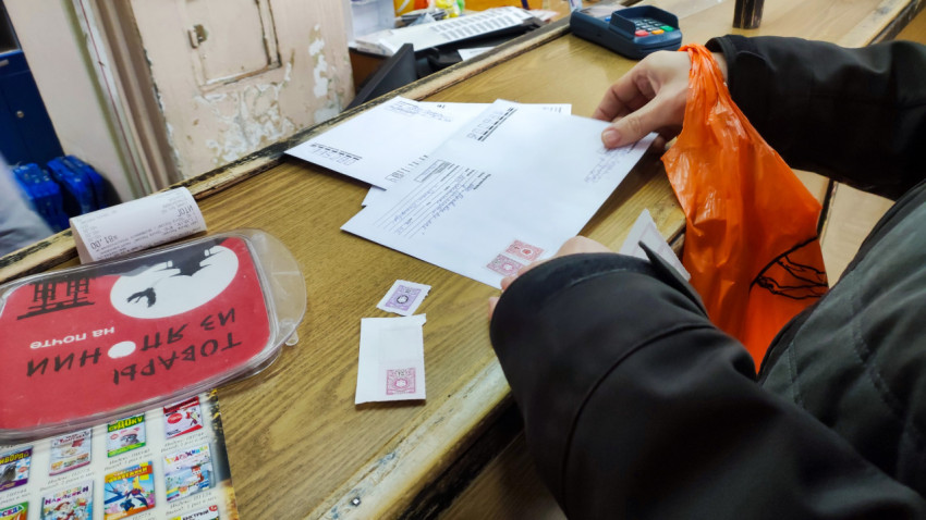 Мужчина приклеивает почтовые марки на письмо в почтовом офисе