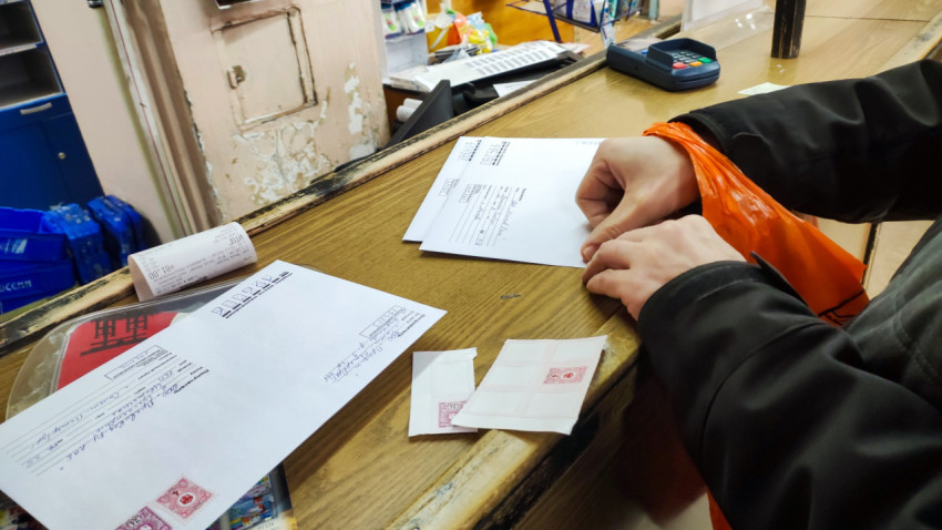 Человек наклеивает марки на конверты в отделении связи