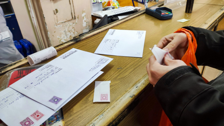 В почтовом отделении мужчина приклеивает марки к конвертам