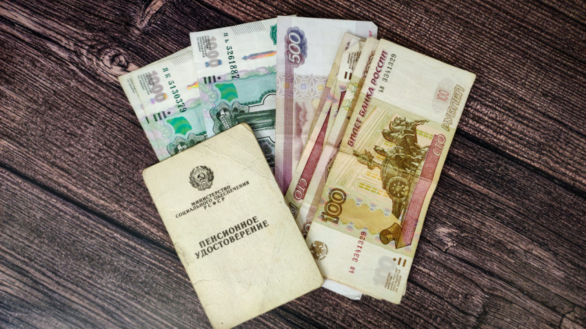 Пенсионное удостоверение и денежные купюры в российских рублях на деревянном столе