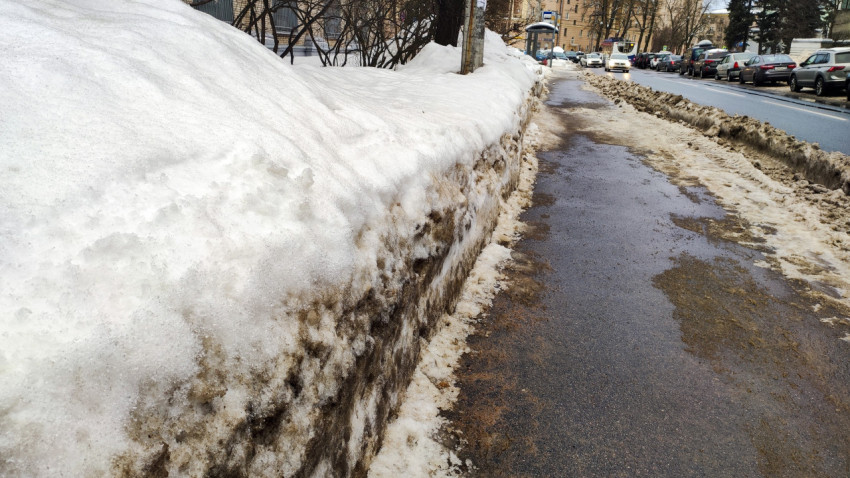 Улица в городе с высокой стеной снега и лужами