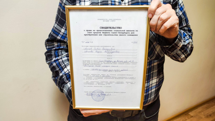Мужчина держит сертификат на покупку квартиры от государства в Санкт-Петербурге