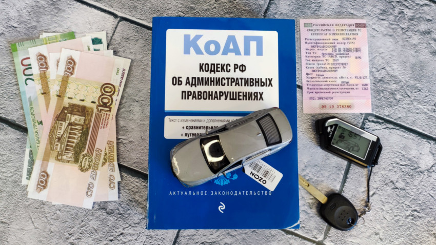 Кодекс об административных правонарушениях с макетом машины, деньгами, СТС и ключами на столе