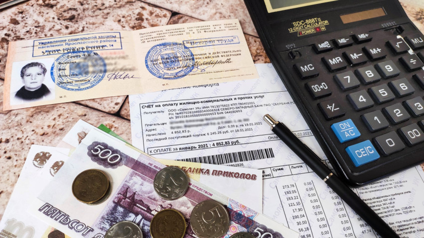 Счет на оплату коммунальных услуг и документы ветерана труда на столе с деньгами и калькулятором