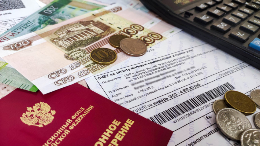 Платежка за жилищно-коммунальные услуги и пенсионное удостоверение на столе с деньгами и калькулятором