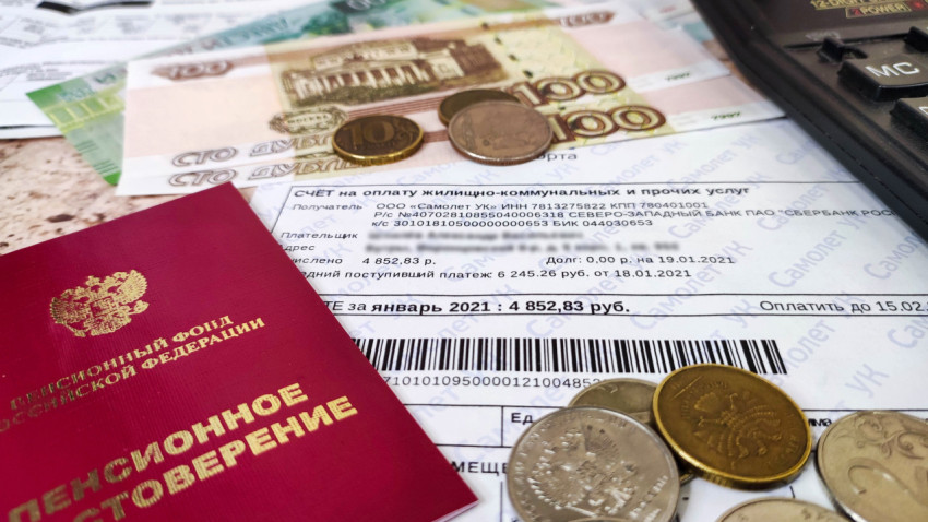 Квитанция по жилищно-коммунальным услугам и пенсионное удостоверение на столе с деньгами и калькулятором