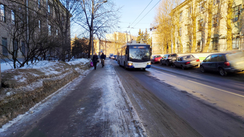 Троллейбус проезжает по улице в городе среди сугробов и автомобилей