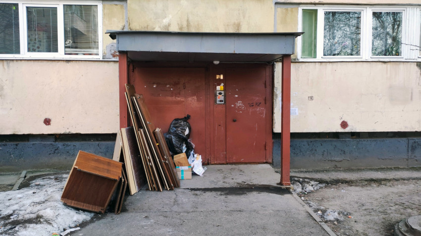 Устаревшая мебель и мусорные пакеты у дверей подъезда многоквартирного дома