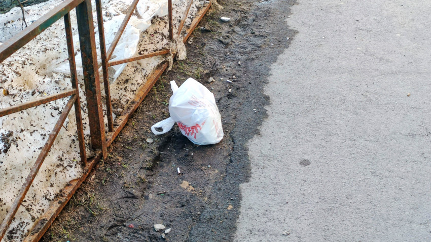 Брошенный мусорный пакет рядом с забором
