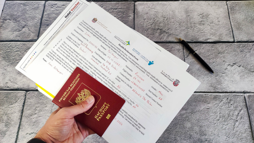 Рука с загранпаспортом, авиабилетами, декларацией здоровья и ваучером отеля