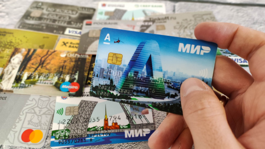 Карта «МИР» в руке на фоне множества банковских карт