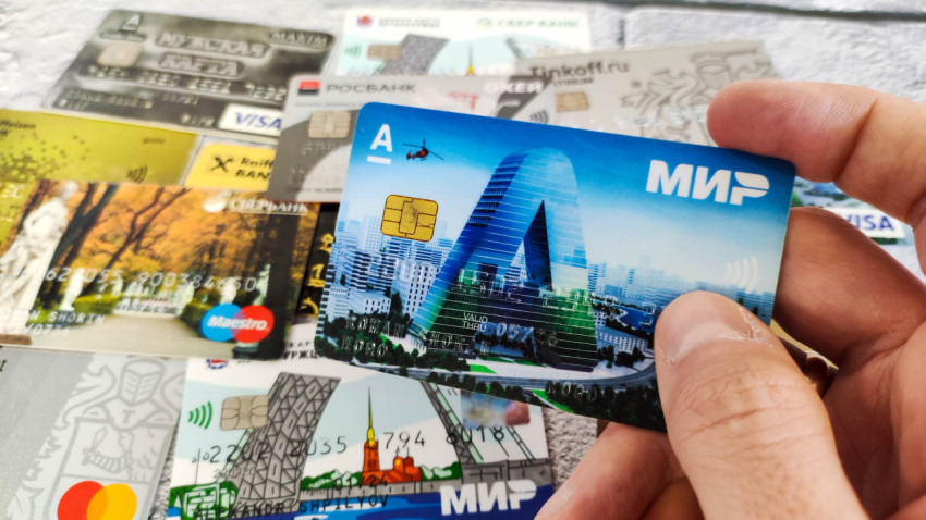 Карта «МИР» в руке на фоне различных банковских карт