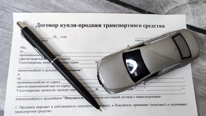 Договор купли-продажи автомобиля с авторучкой и моделью машины на сером фоне