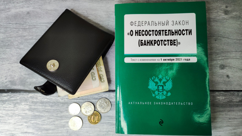 Кошелёк с деньгами и книга о банкротстве на деревянном фоне