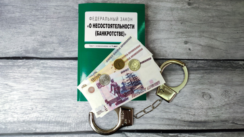 Книга о банкротстве, наручники и купюры на столе