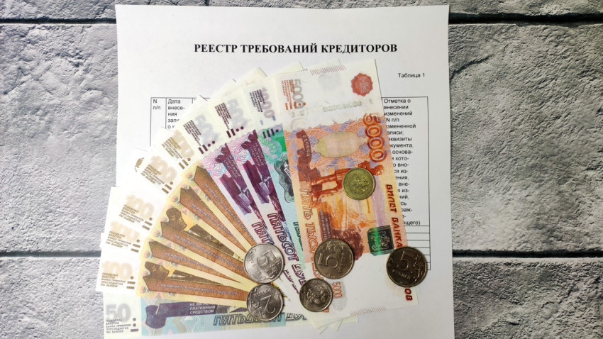 Разноцветные купюры и монеты на фоне реестра требований кредиторов