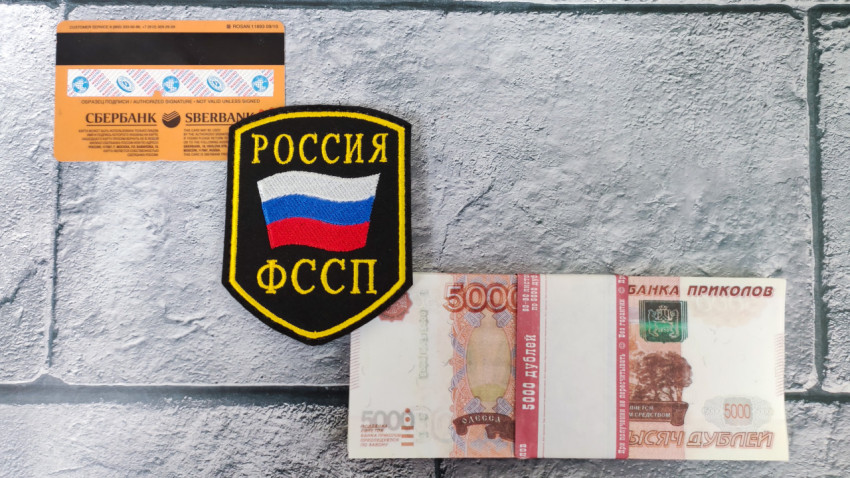 Шеврон ФССП и банковская карта рядом с купюрами банка приколов