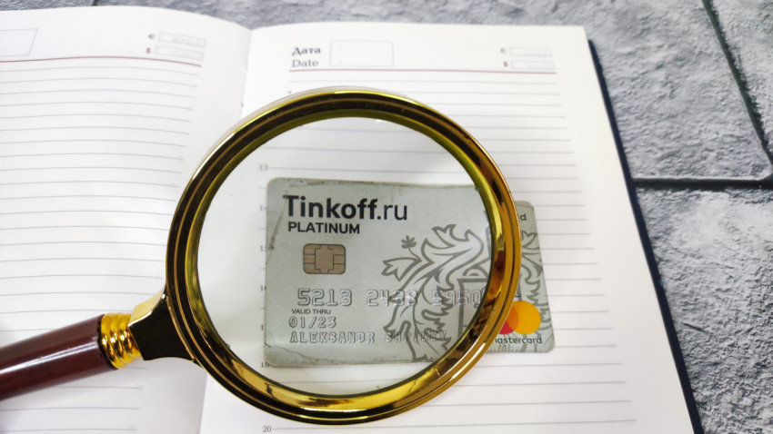 Банковская карта Tinkoff под лупой на фоне ежедневника
