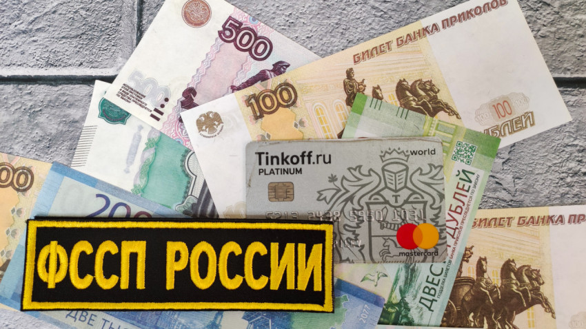 Карта Tinkoff и шеврон ФССП на фоне российских купюр
