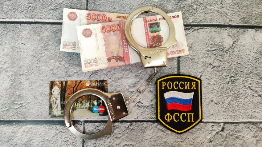 Наручники, деньги и карта на фоне шеврона ФССП