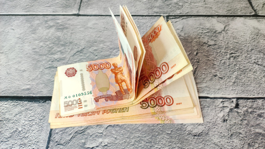 Пачка пятитысячных купюр на сером фоне в развёрнутом виде