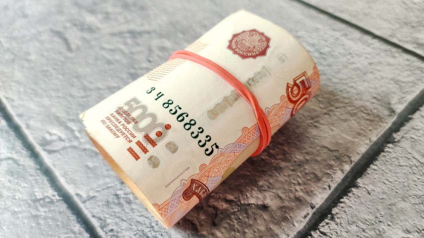 Скрутка российских банкнот с резинкой на фоне плитки