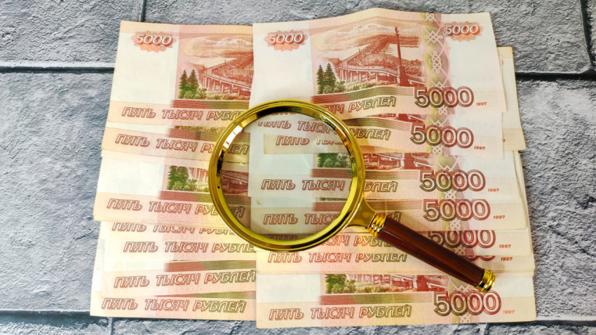 Лупа на фоне банкнот номиналом 5000 рублей