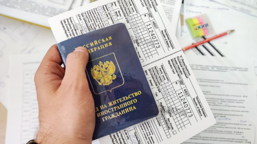 Вид на жительство и миграционная карта в руке на фоне бумаг