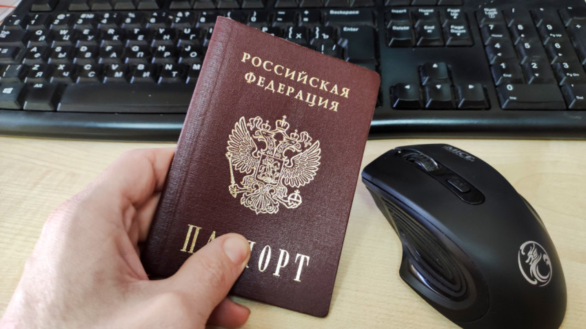 Паспорт РФ в руке рядом с мышью и клавиатурой