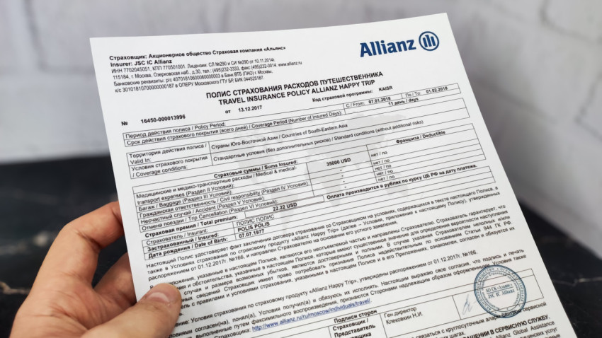 Полис Allianz Happy Trip в руке на мраморной поверхности