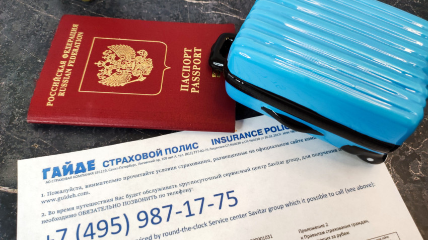 Чемодан и паспорт на фоне страхового полиса GUIDEH