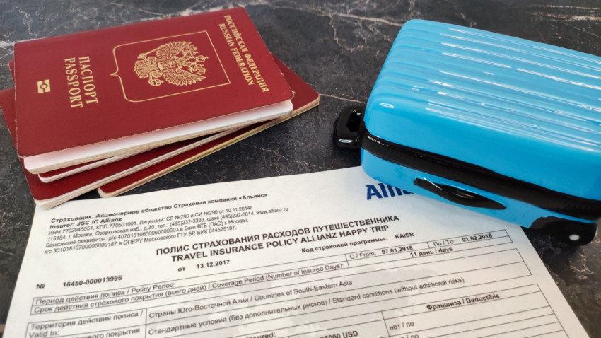 Загранпаспорта, страховой полис и мини-чемодан на мраморной поверхности