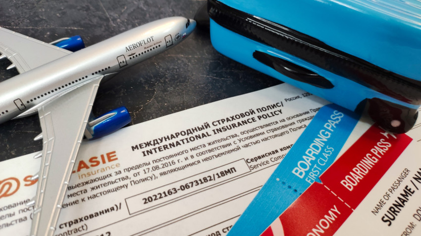 Миниатюрный самолёт и чемодан рядом с международным страховым полисом