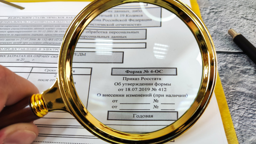 Рука с лупой над статистической формой 4-ОС о затратах на охрану окружающей среды