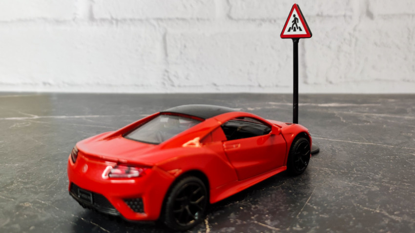 Игрушечный автомобиль стоит рядом с дорожным знаком пешеходного перехода